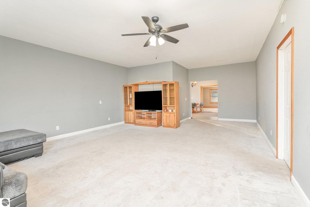 Spacious living room in Mt. Pleasant home featuring light gray walls, plush carpet, a ceiling fan, and a wooden entertainment unit with a television, showcasing versatile multi-use space.