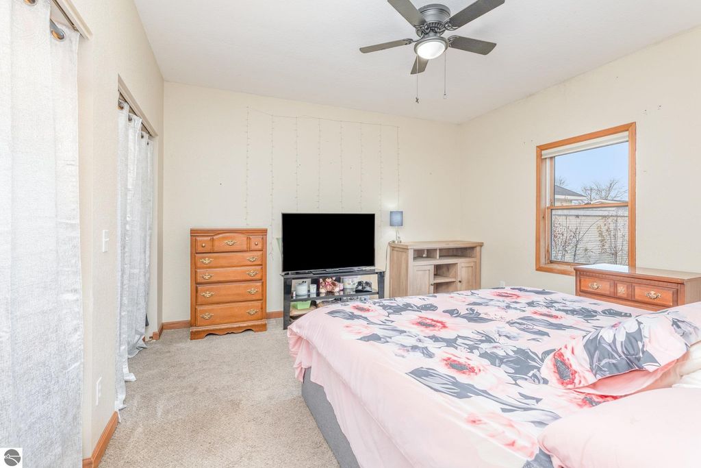 Spacious bedroom at 1708 W Lyons Street, featuring a floral bedspread, wooden dresser, and a TV stand, with natural light from a window and light-colored walls.