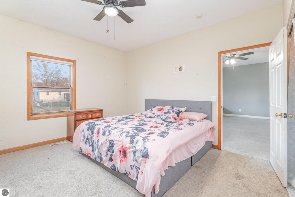 Spacious bedroom featuring a floral-patterned bedspread, wooden furniture, and a window overlooking a yard, part of the 1708 W Lyons Street listing in Mt. Pleasant, MI.