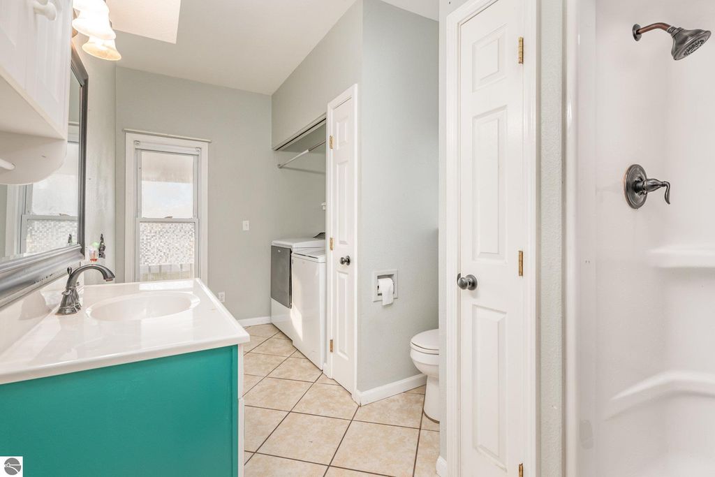 Bright laundry room with white cabinetry, turquoise countertop, and tiled floor, showcasing washing machine, shower, and bathroom door, in the home at 1708 W Lyons Street, Mt Pleasant, MI.