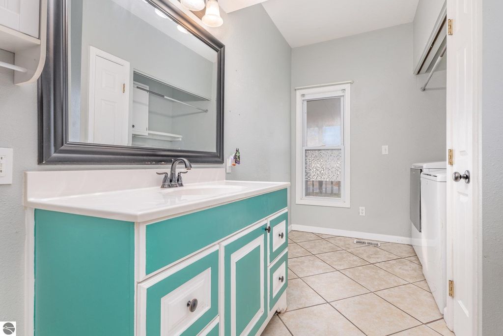 Bathroom interior featuring a turquoise vanity with white accents, large mirror, and tiled floor, showcasing a spacious and well-lit area in the home at 1708 W Lyons Street, Mt Pleasant, MI.