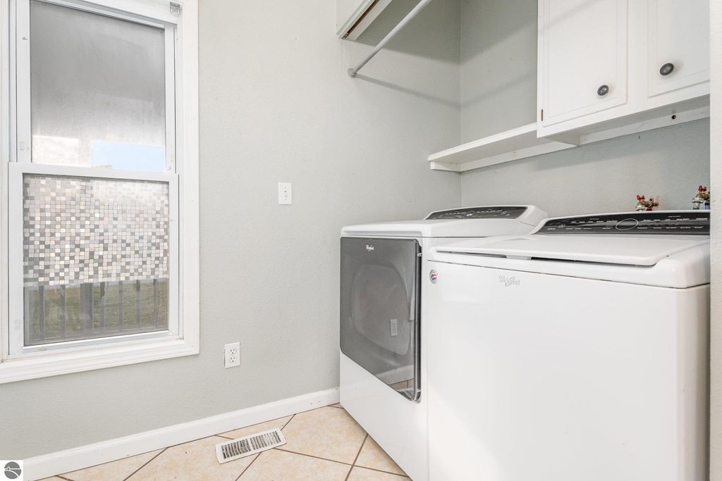 Laundry room featuring a Whirlpool washer and dryer, tiled floor, and window with decorative film, emphasizing functional space in the 1708 W Lyons Street property.