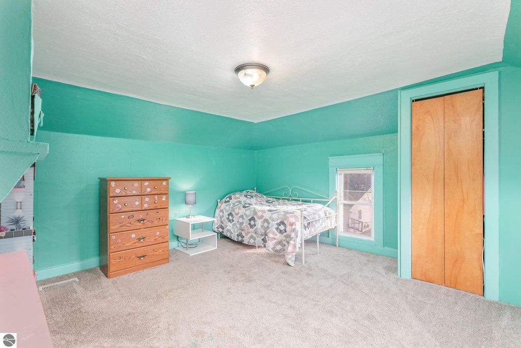 Spacious bedroom with teal walls, carpeted flooring, a wooden dresser, a nightstand, and a double bed, highlighting versatile living space in the property at 1708 W Lyons Street, Mt Pleasant, MI.