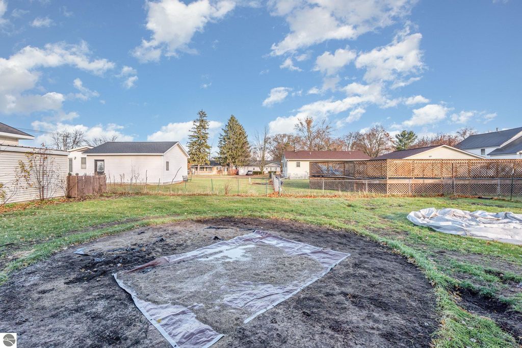 Backyard view of 1708 W Lyons Street in Mt. Pleasant, featuring a grassy area, neighboring homes, and a tarp on the ground, highlighting the property's outdoor space and potential for landscaping.