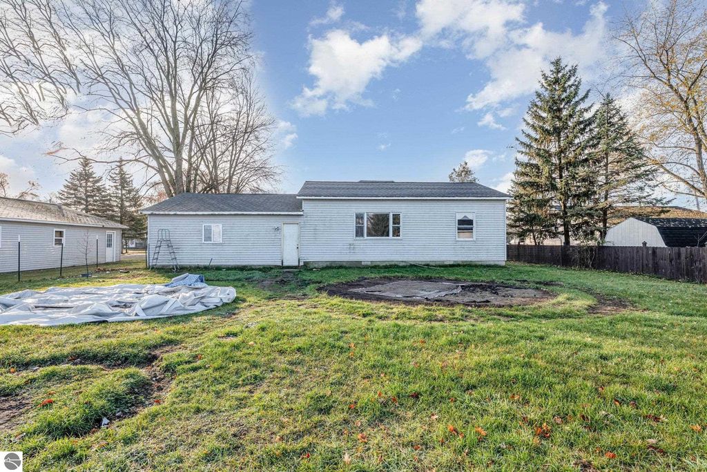 Spacious backyard view of 1708 W Lyons Street in Mt. Pleasant, featuring a home with a light-colored exterior, large yard, and surrounding trees, ideal for potential buyers exploring real estate options.