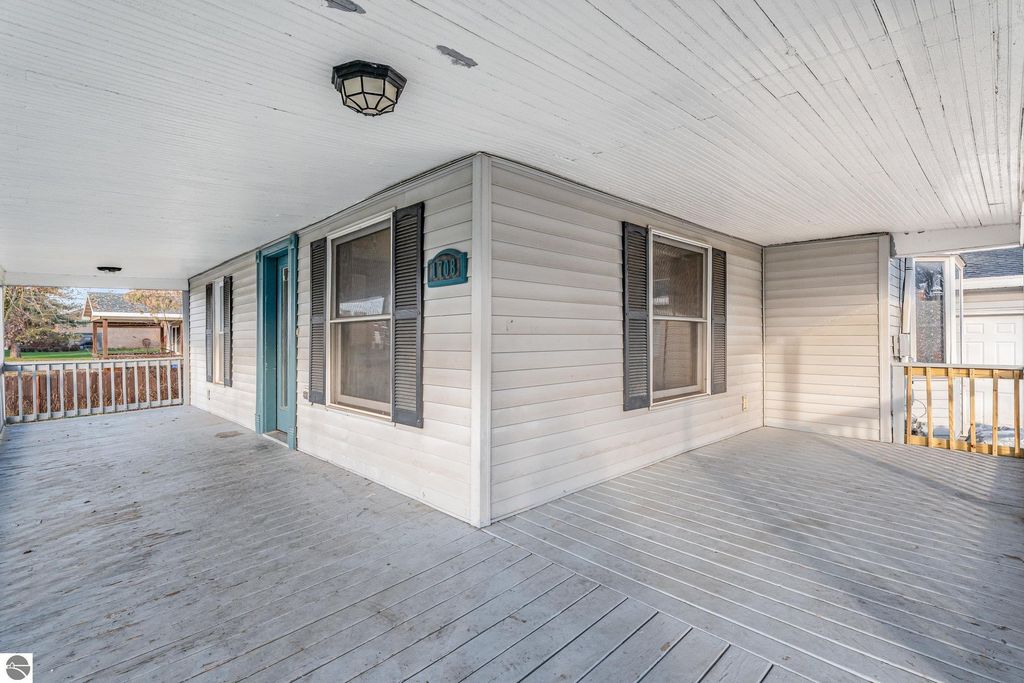Covered porch of 1708 W Lyons Street, Mt Pleasant, MI, featuring light-colored wood flooring, blue door, and black shutters, showcasing the property's inviting entrance and outdoor space.