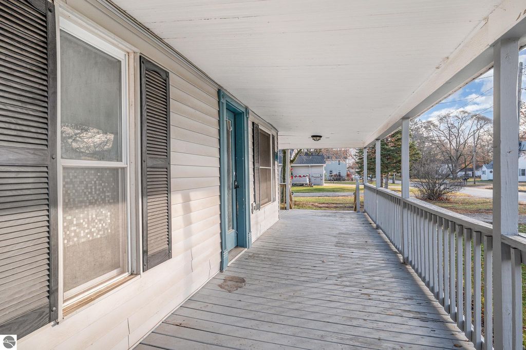 Wrap-around covered porch of the home at 1708 W Lyons Street, Mt Pleasant, featuring wooden railing, blue door, and nearby yard space.