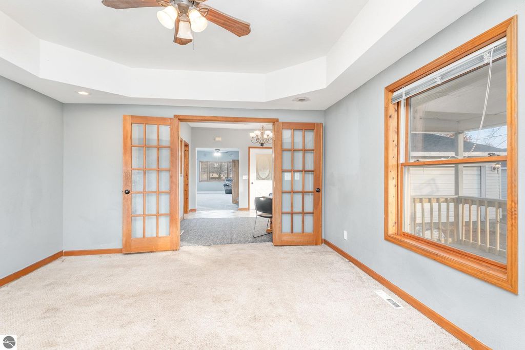 Spacious living area of 1708 W Lyons Street, featuring light gray walls, wooden French doors, and large windows with natural light, showcasing versatile multi-use space for living and dining.
