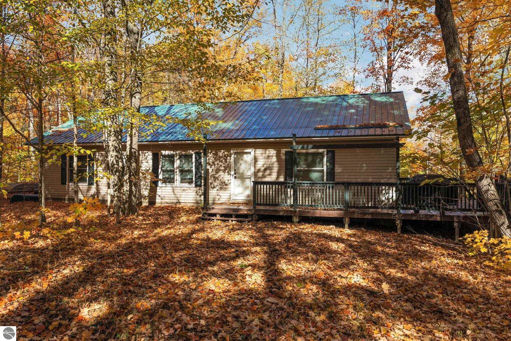 3-bedroom, 2-bath home with a metal roof, surrounded by autumn foliage and a wooden deck, located on a corner lot in Blue Lake Heights, Kalkaska, MI.