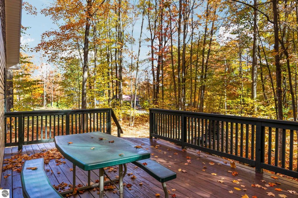 Deck with green picnic table surrounded by autumn foliage in Blue Lake Heights, Kalkaska, MI, showcasing outdoor living space near North Blue Lake.