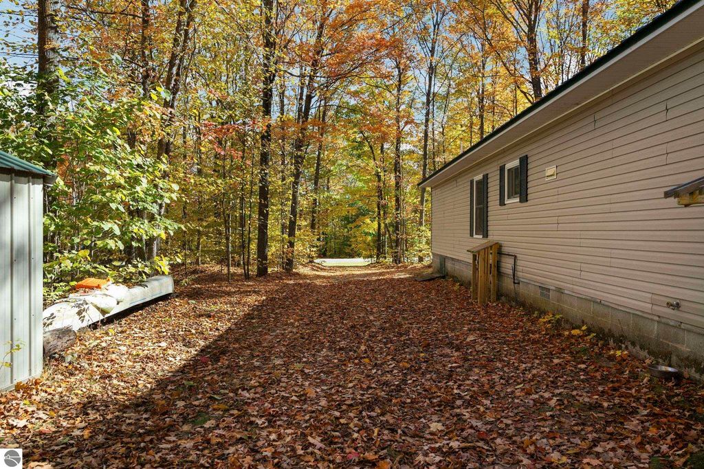 Pathway lined with autumn leaves leading to a 3-bedroom home in a wooded setting near Blue Lake Heights, Kalkaska, MI, showcasing natural charm and tranquility.