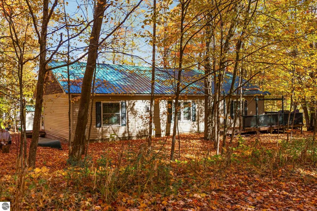 3-bedroom, 2-bath home with a blue metal roof, surrounded by autumn foliage, located on a corner lot in Blue Lake Heights, Kalkaska, MI.