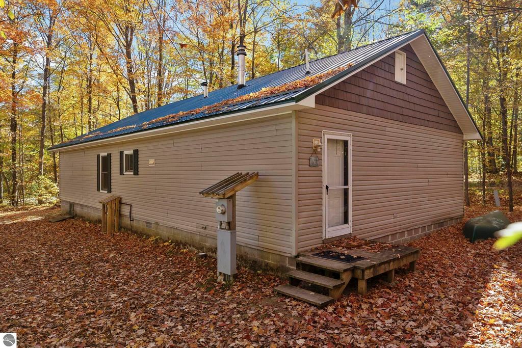 3-bedroom, 2-bath home exterior on wooded lot in Blue Lake Heights, featuring new metal roof, surrounded by autumn foliage and fallen leaves.