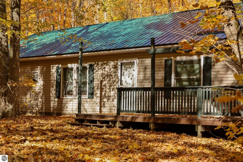 3-bedroom home with a green metal roof and wooden deck surrounded by autumn foliage in Blue Lake Heights, Kalkaska, MI, highlighting outdoor living and serene natural setting.