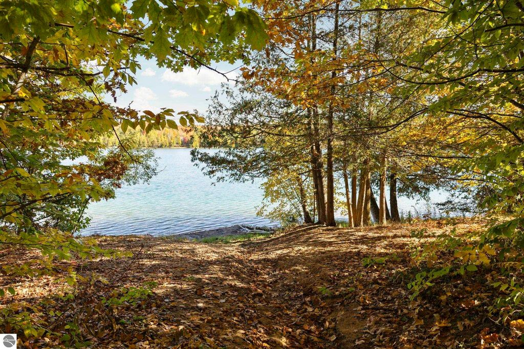 Scenic view of North Blue Lake framed by autumn foliage, showcasing tranquil waters and natural beauty, highlighting the outdoor lifestyle near 7149 W Blue Lake Road, Kalkaska, MI.