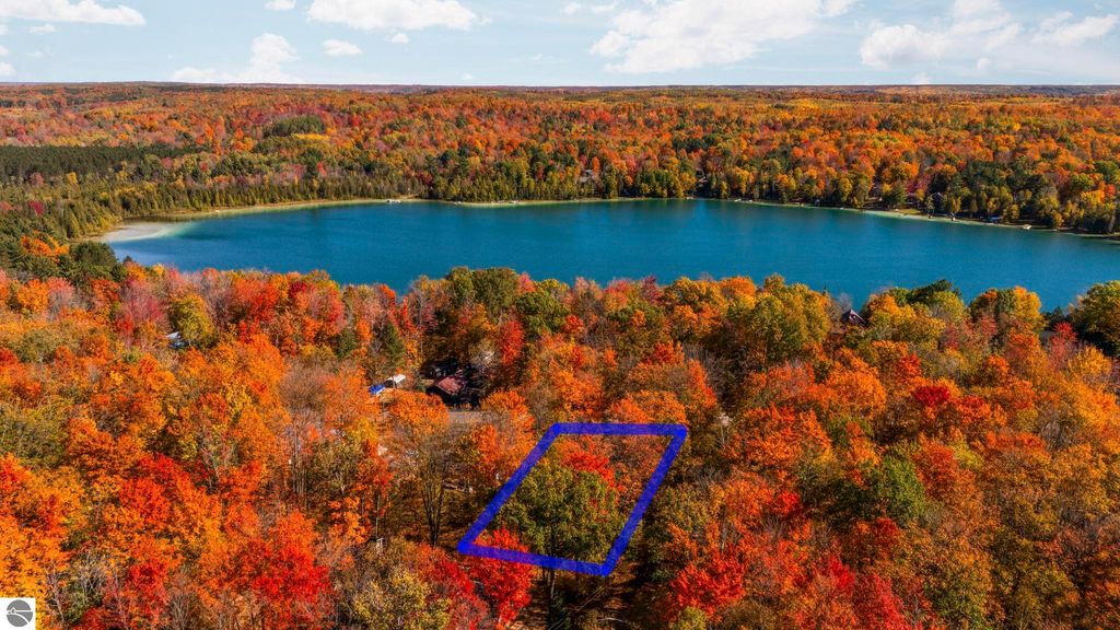 Aerial view of vibrant fall foliage surrounding a tranquil blue lake, highlighting the corner lot at 7149 W Blue Lake Road, NE, in Kalkaska, MI, showcasing the natural beauty and recreational opportunities of the Blue Lake Heights community.