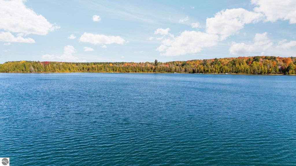 Scenic view of North Blue Lake, surrounded by colorful autumn foliage and clear blue skies, highlighting the natural beauty and tranquility of the Blue Lake Heights community in Kalkaska, MI.