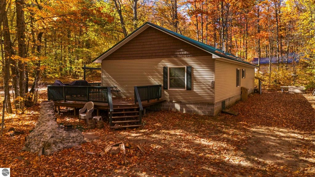 3-bedroom, 2-bath home with a wooden deck, surrounded by fall foliage in Kalkaska, MI, featuring a stone fireplace and a serene outdoor setting.