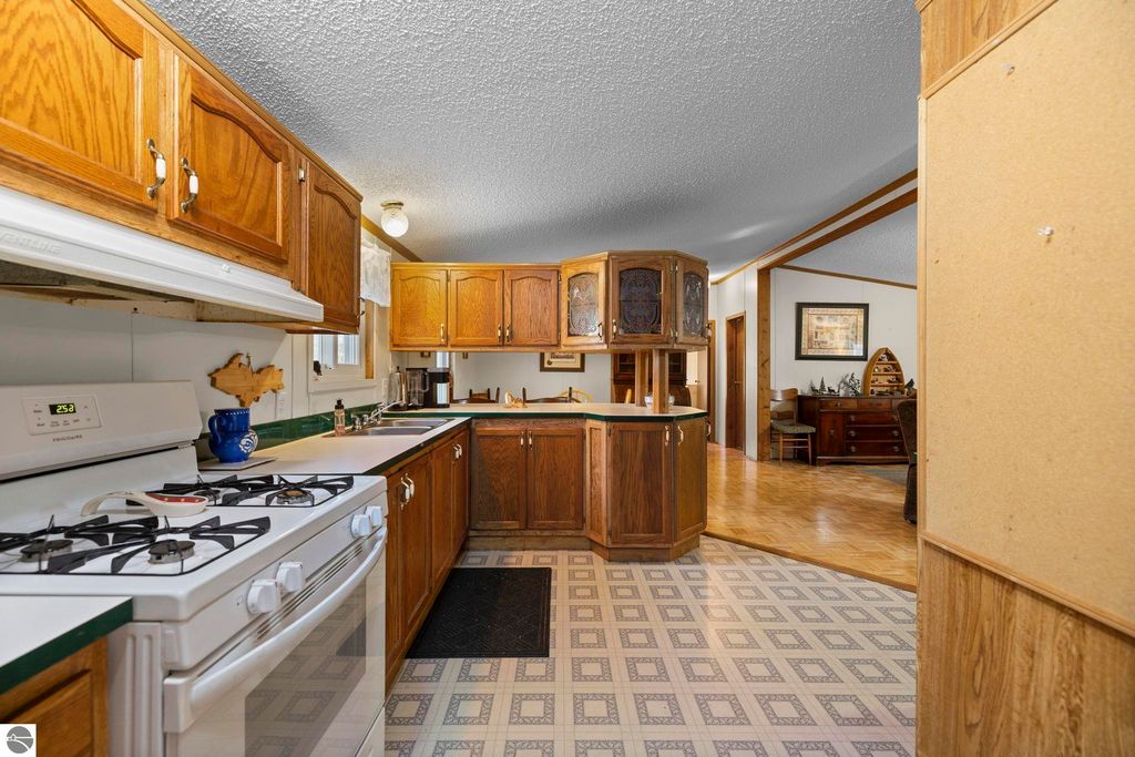 Kitchen interior featuring wooden cabinets, gas stove, and countertop, showcasing spacious layout and natural light, ideal for family living in Kalkaska, MI home.