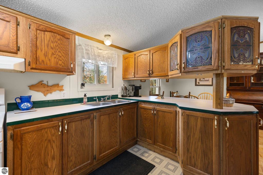 Inviting kitchen with wooden cabinetry, green countertops, and natural light from window, featuring a sink, stove, and decorative elements, highlighting the cozy atmosphere of the home at 7149 W Blue Lake Road, Kalkaska, MI.