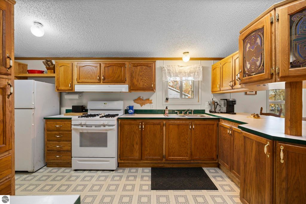 Kitchen interior featuring wooden cabinets, white gas stove, and refrigerator, showcasing a cozy and functional space in a 3-bedroom home for sale in Kalkaska, MI.