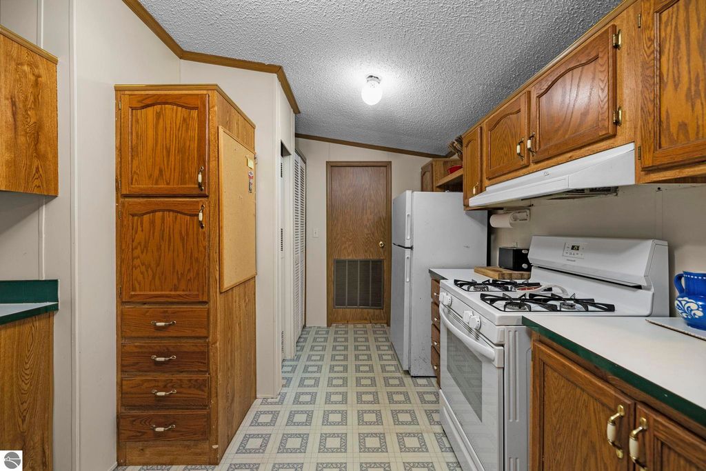Kitchen interior featuring wooden cabinetry, gas stove, and refrigerator, showcasing the inviting atmosphere of the 3-bedroom, 2-bath home for sale at 7149 W Blue Lake Road in Kalkaska, MI.
