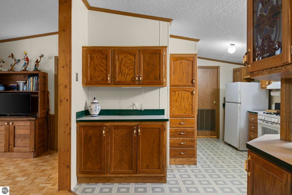 Interior view of a kitchen featuring wooden cabinets, green countertop, and appliances, highlighting the cozy living space of the 3-bedroom, 2-bath home at 7149 W Blue Lake Road, Kalkaska, MI.