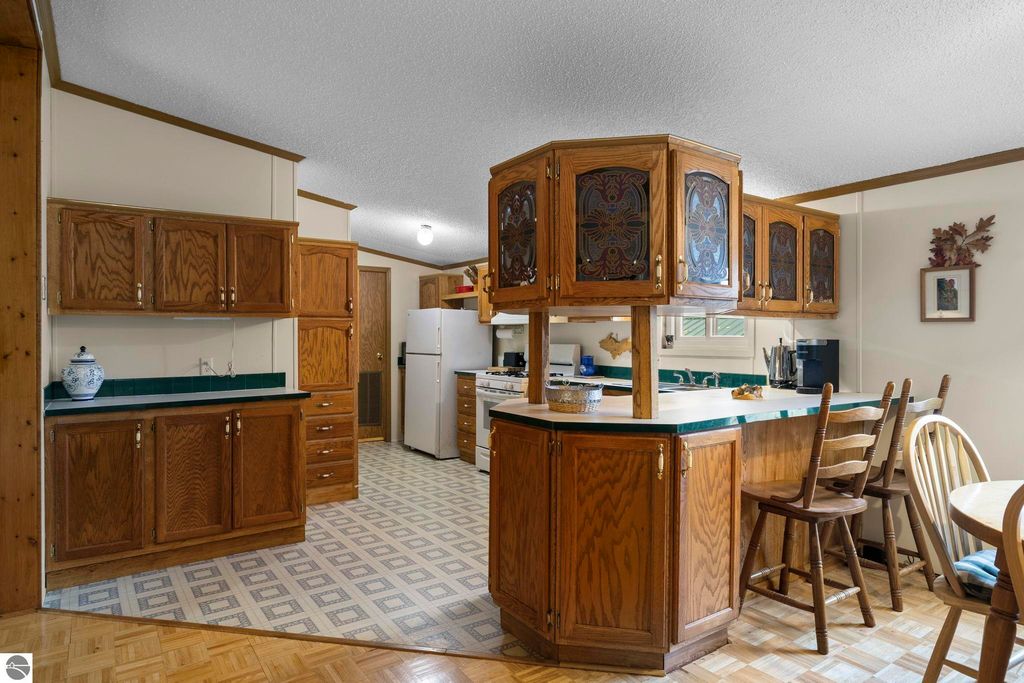 Kitchen interior featuring wooden cabinetry, green countertops, and a dining area with wooden chairs, showcasing a cozy and inviting atmosphere in the home at 7149 W Blue Lake Road, Kalkaska, MI.