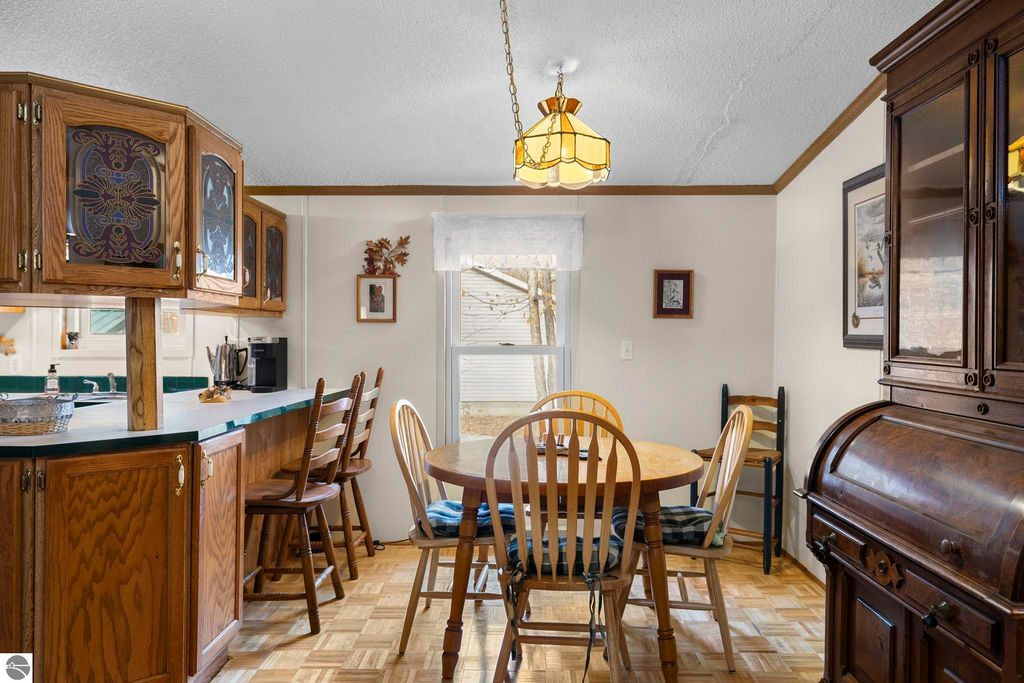 Cozy kitchen and dining area featuring wooden cabinetry, a round table with chairs, and a window providing natural light, showcasing the welcoming interior of the 3-bedroom home at 7149 W Blue Lake Road, Kalkaska, MI.
