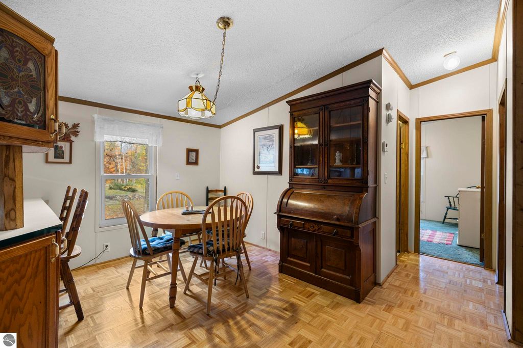 Dining area featuring a round table with wooden chairs, a vintage wooden hutch, and large windows allowing natural light, showcasing the inviting interior of a 3-bedroom, 2-bath home for sale in Kalkaska, MI.