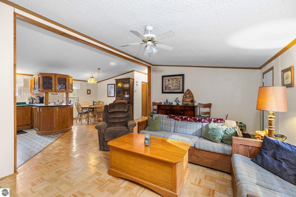 Cozy living room interior featuring a plaid sofa, wooden coffee table, and open layout connecting to the kitchen, highlighting the inviting atmosphere of the home at 7149 W Blue Lake Road, Kalkaska, MI.