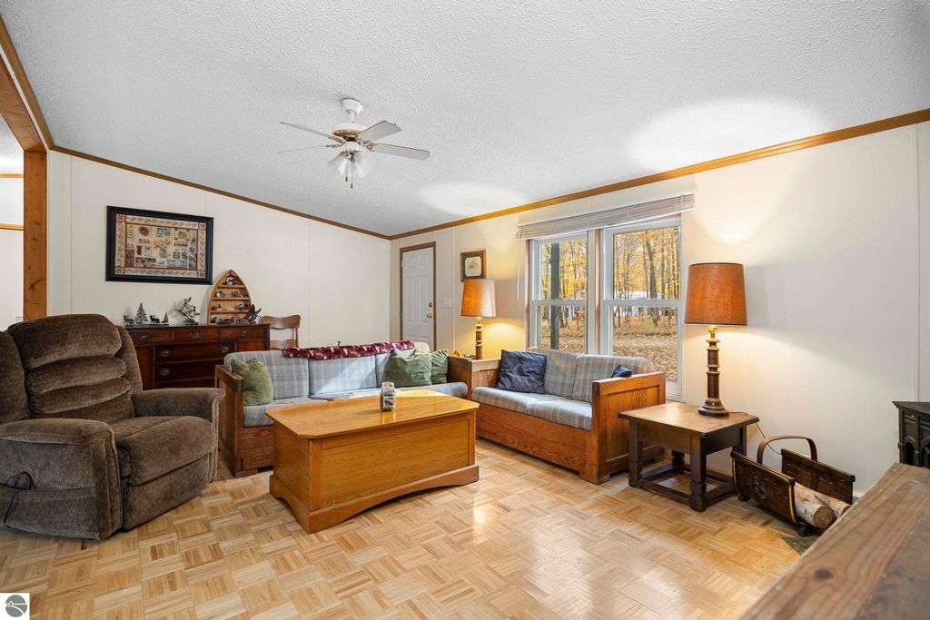 Cozy living room with wooden furniture, plush seating, and large windows showcasing autumn scenery, highlighting the inviting atmosphere of the 3-bedroom, 2-bath home at 7149 W Blue Lake Road, Kalkaska, MI.