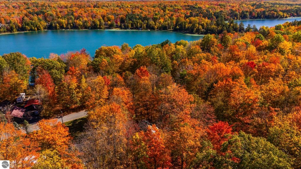 Aerial view of vibrant autumn foliage surrounding North Blue Lake, featuring colorful trees in shades of orange, red, and yellow, with calm blue waters reflecting the landscape, highlighting the natural beauty of the Blue Lake Heights community in Kalkaska, MI.