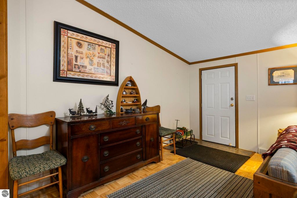 Interior view of a cozy entryway featuring a wooden dresser with decorative items, a framed artwork, and a white door, emphasizing the inviting atmosphere of the 3-bedroom home for sale at 7149 W Blue Lake Road, Kalkaska, MI.