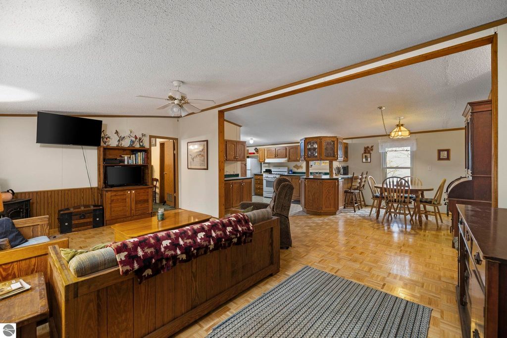 Cozy living room with wooden accents, featuring a sofa, television, and a view into the kitchen and dining area, showcasing an open layout ideal for family gatherings in a home near Blue Lake in Kalkaska, MI.