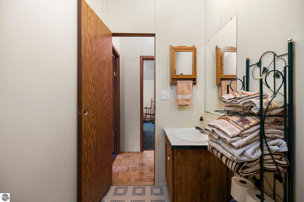 Bathroom interior featuring wooden cabinetry, stacked towels, and mirrors, with a doorway leading to another room in a 3-bedroom home for sale at 7149 W Blue Lake Road, Kalkaska, MI.