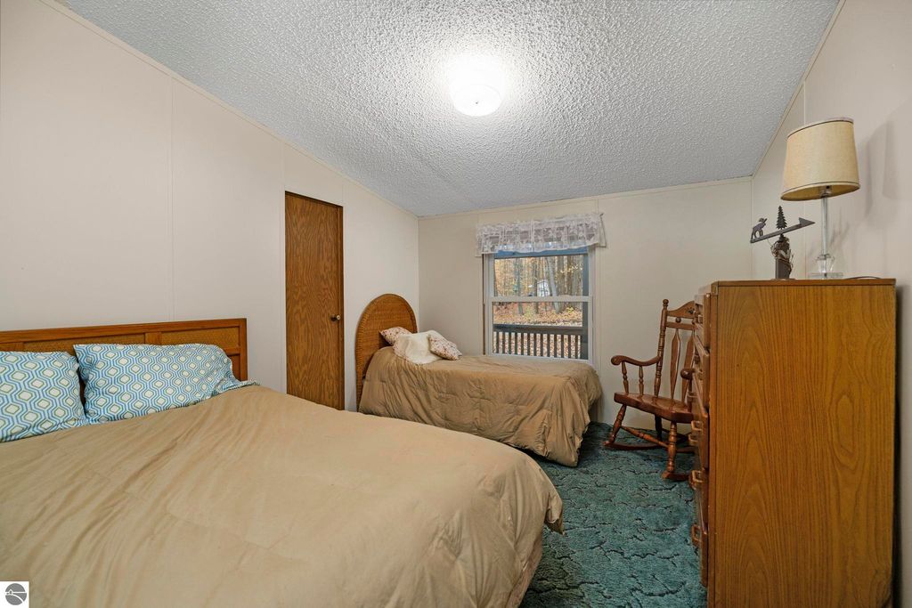 Cozy bedroom featuring two beds with beige bedding, wooden furniture, and a window overlooking a wooded area, reflecting the inviting atmosphere of the home at 7149 W Blue Lake Road, Kalkaska, MI.