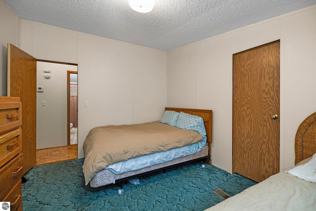 Cozy bedroom featuring a double bed with blue polka dot bedding, wooden furniture, and a door leading to an adjoining room, showcasing the inviting interior of the home at 7149 W Blue Lake Road, Kalkaska, MI.