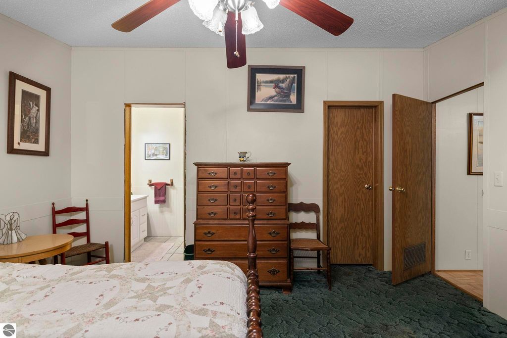 Cozy bedroom featuring a wooden dresser, red accent chair, and a round table, with doors leading to a bathroom and closet, adorned with framed artwork and a ceiling fan.