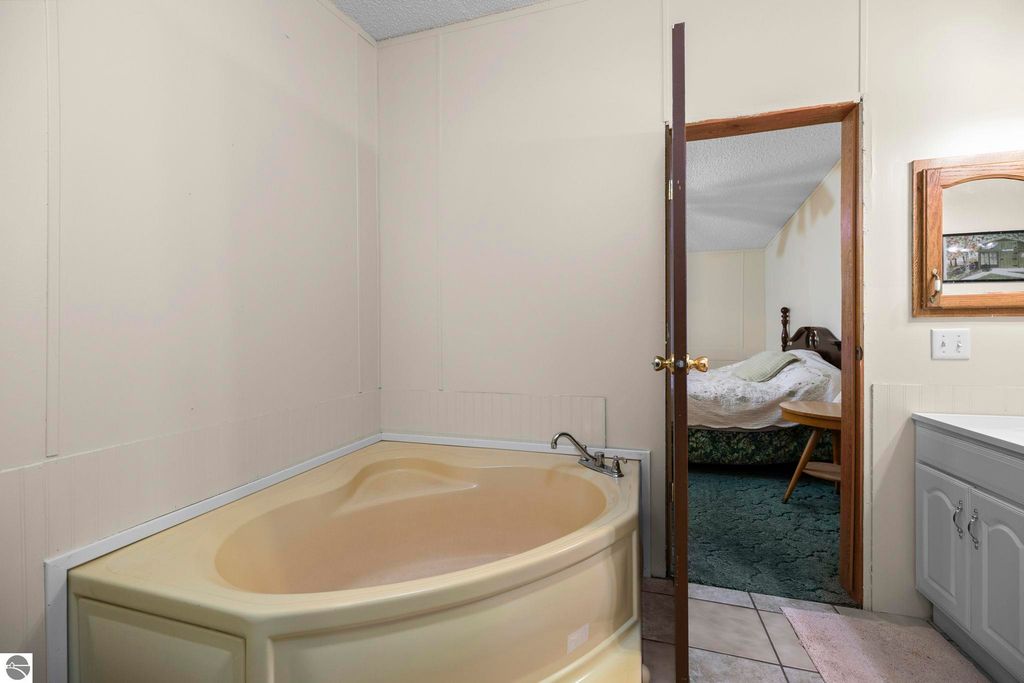 Bathroom featuring a corner jetted tub, beige walls, and a doorway leading to a bedroom with a bed, highlighting the home's interior comfort and design.