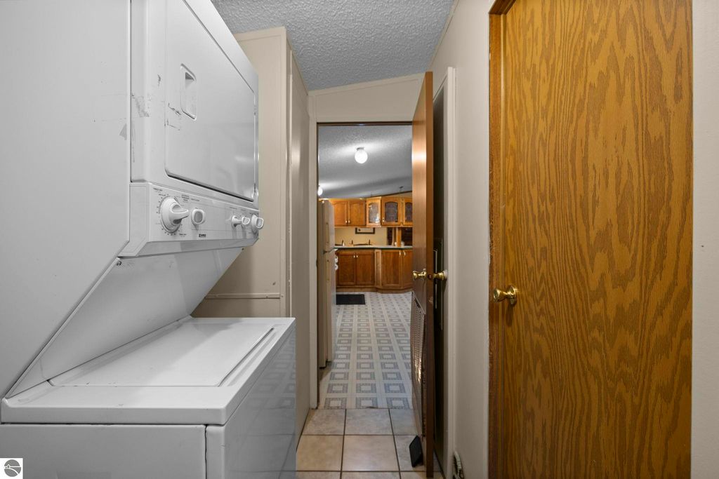 Washer and dryer unit in a hallway leading to a kitchen with wooden cabinets, beige walls, and tiled flooring, showcasing the home's functional layout and modern amenities.