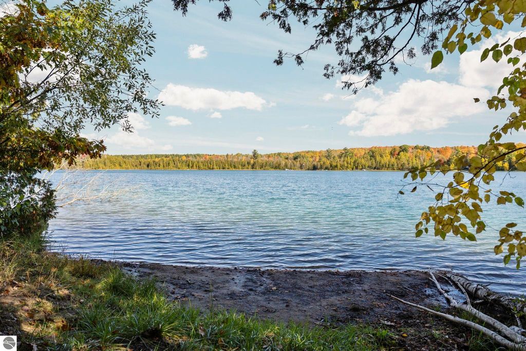 Scenic view of North Blue Lake surrounded by colorful autumn foliage, showcasing calm waters ideal for swimming and fishing, highlighting the natural beauty of the Blue Lake Heights community in Kalkaska, MI.