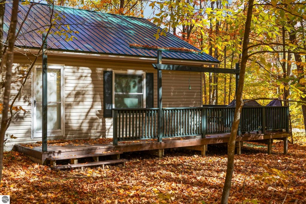 Cozy 3-bedroom home with a green metal roof and spacious deck, surrounded by vibrant autumn foliage in Blue Lake Heights, Kalkaska, MI.