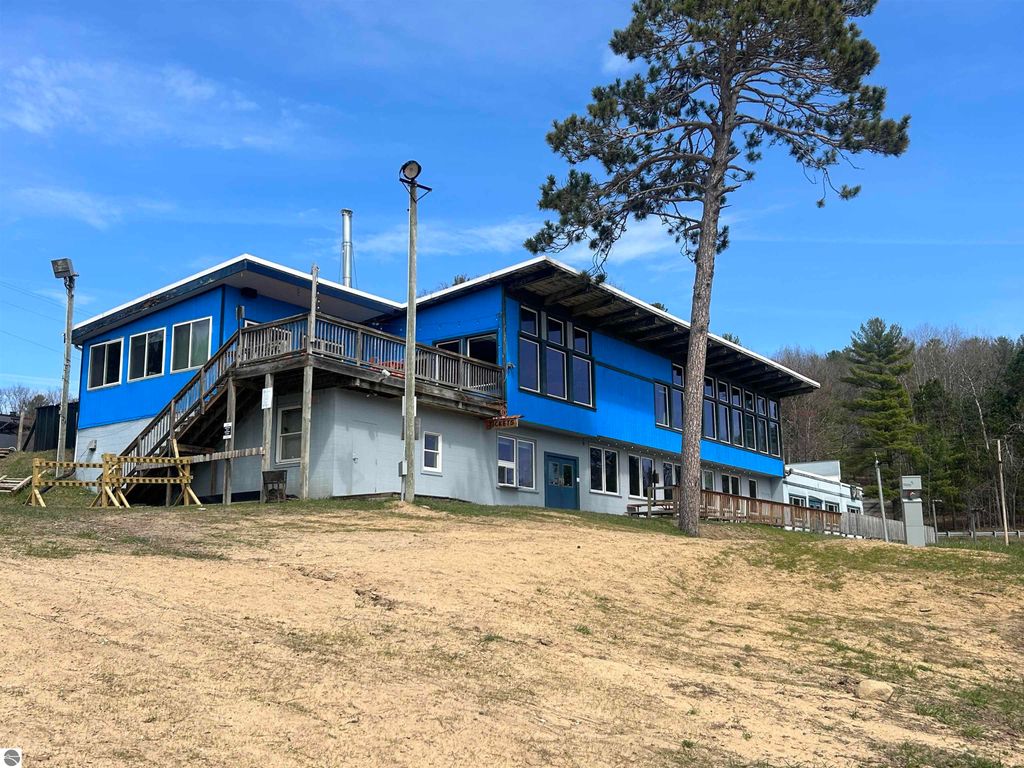 Custom blue home on wooded lot in Traverse City, featuring large windows, deck, and surrounding greenery, ideal for nature lovers.