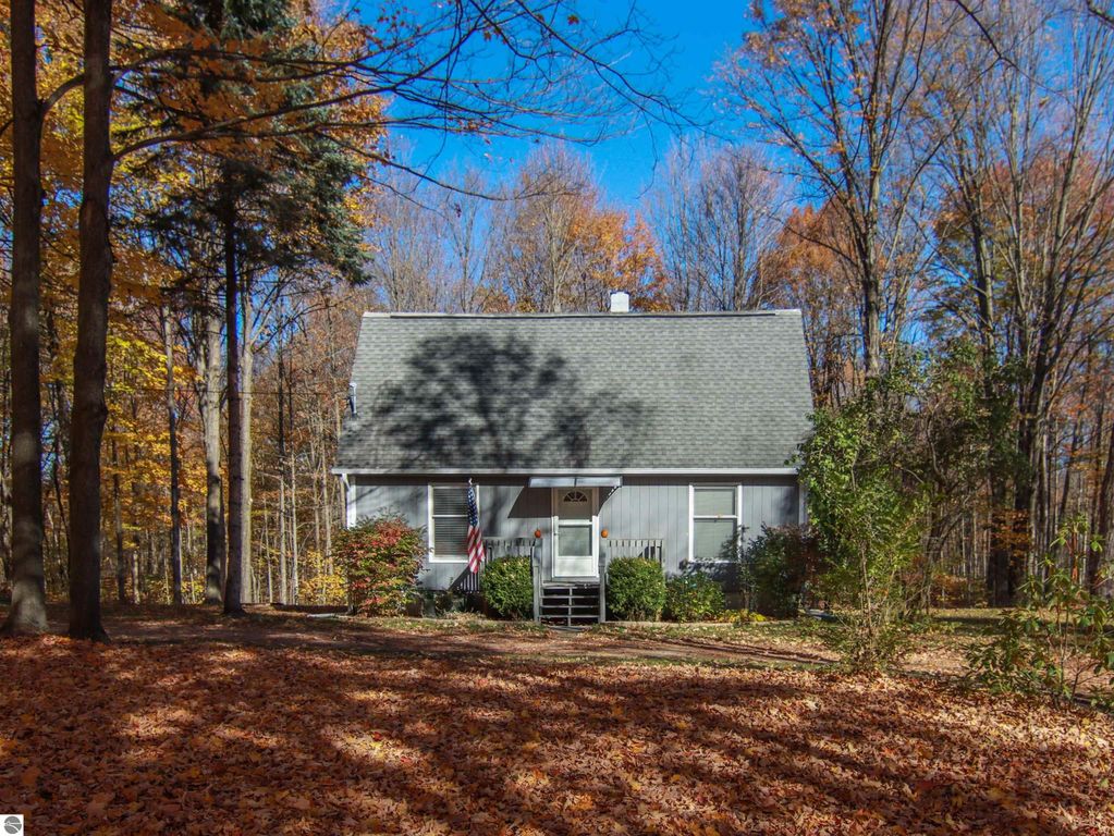 Saltbox style home surrounded by autumn foliage on 8.75 acres, featuring a welcoming front entrance with steps and an American flag, located at 20280 Cadillac Highway, Copemish, MI.