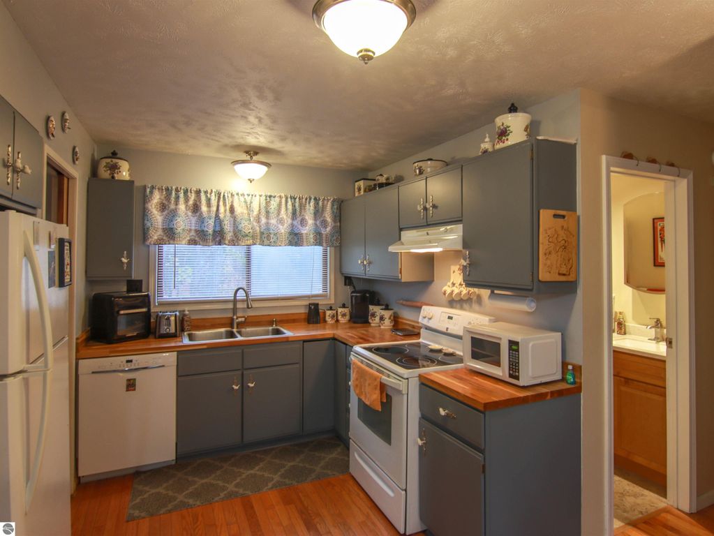 Cozy kitchen with gray cabinets, wooden countertops, and modern appliances, featuring a window with patterned curtains and a view of the adjoining bathroom.