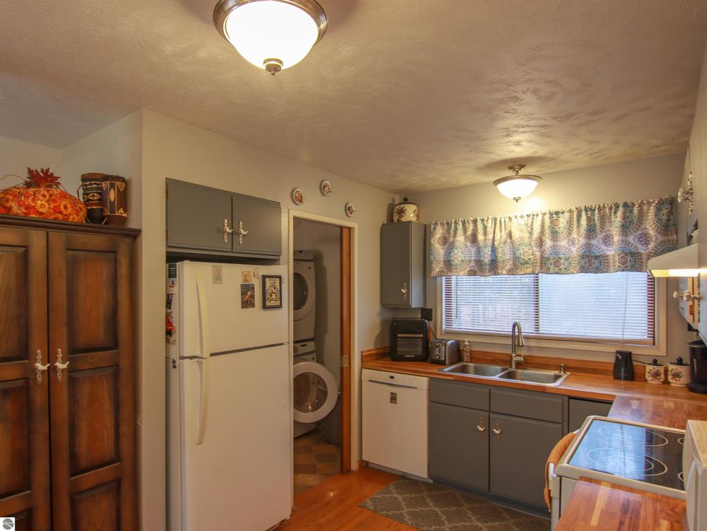 Welcoming kitchen in a saltbox style home, featuring wood cabinets, modern appliances, and a sunlit window with a patterned curtain, highlighting the cozy living space in Copemish, MI.