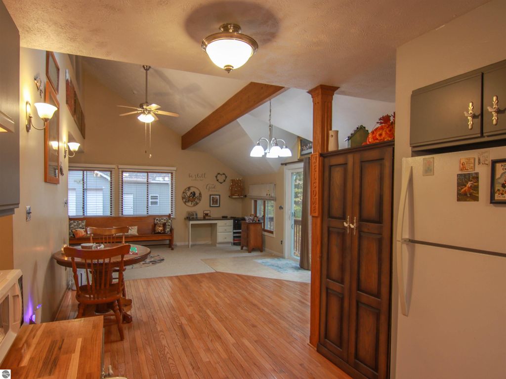 Welcoming interior of a saltbox style home featuring a woodstove, dining area, and kitchen with hardwood floors, showcasing natural light and cozy furnishings.
