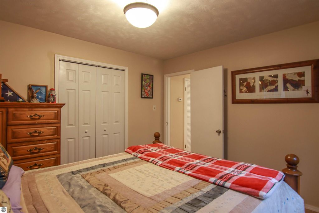 Cozy bedroom featuring a wooden dresser, bed with a plaid blanket, and double closet doors, showcasing a warm, inviting atmosphere in the 3-bedroom, 2-bath home for sale in Copemish, MI.