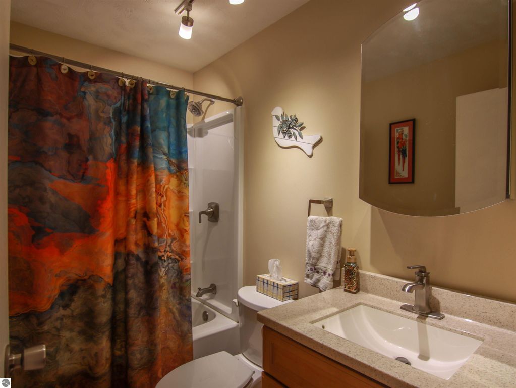 Bathroom featuring a colorful shower curtain, modern sink, and mirror, showcasing a cozy and inviting atmosphere in the 3-bed, 2-bath home for sale in Copemish, MI.